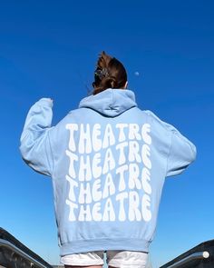 a woman standing on top of a bridge with her back to the camera, wearing a blue hoodie that says theatre theatre