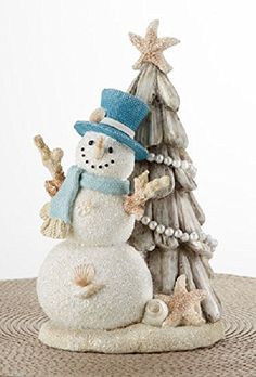 a snowman next to a small christmas tree on a table with starfish around it