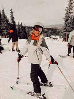 a woman on skis in the snow with other skiers behind her and trees