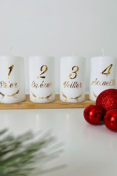 three white candles with gold numbers on them sitting next to christmas ornaments and a red bauble