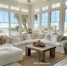 a living room filled with lots of white furniture next to large windows on top of a wooden floor