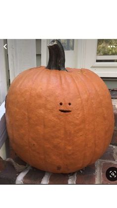 a pumpkin sitting on top of a brick floor next to a door with a face drawn on it