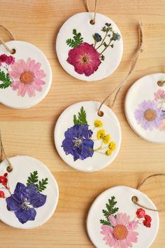 four ceramic flower ornaments hanging from twine on a wooden table with string attached to each ornament