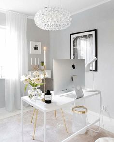 a white desk with a computer on it and flowers in the vase next to it