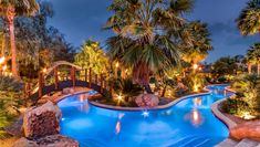 an outdoor swimming pool surrounded by palm trees and landscaping at night with lights on the water