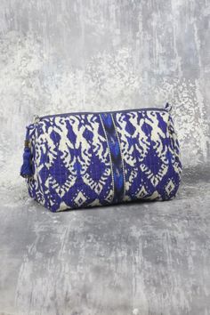 a blue and white clutch bag sitting on top of a cement floor next to a wall