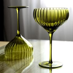 two green wine glasses sitting on top of a wooden table next to eachother