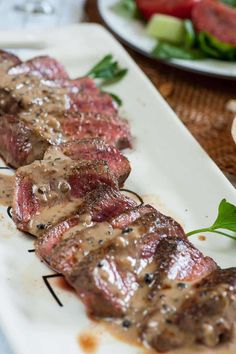 steak with sauce on it sitting on a white plate next to a bowl of salad