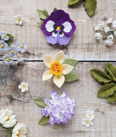 three felt flowers are sitting on a wooden surface with leaves and flowers around them,