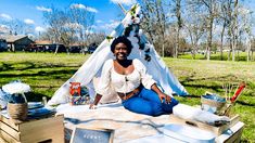 a woman sitting in front of a teepee with food on it and decorations around her