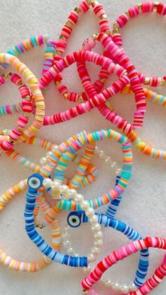 several colorful bracelets are arranged on a white surface with pearls and beads around them