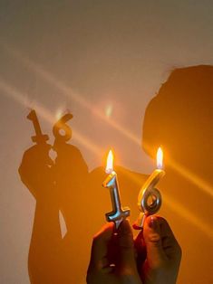 the shadow of a person holding a pair of scissors in front of their face with two lit candles