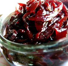 a glass jar filled with red fruit sitting on top of a table