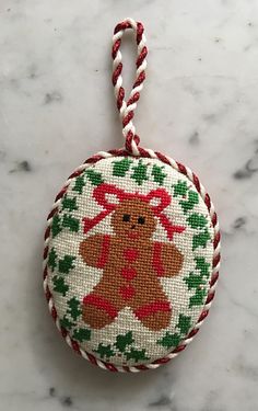 a cross stitch ornament with a teddy bear on it's back hanging from a rope