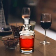 a glass of wine next to a decanter and bowl of nuts on a table