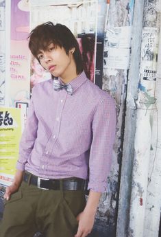 a young man wearing a bow tie standing in front of a wall with posters on it