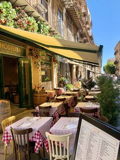 an outdoor restaurant with tables and chairs on the side walk next to a building that has flowers hanging from it