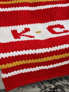 a red and white knitted blanket sitting on top of a bed next to a pillow