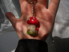 a hand holding a keychain with a mushroom on it's end and a green ball hanging from the middle