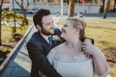 a bride and groom hugging each other on the sidewalk in front of a park area