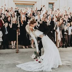 a bride and groom kissing in front of a large group of people holding their hands up