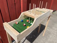 a wooden table with balls and tees in the grass on top, next to a red fence