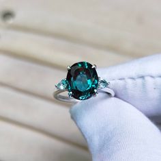 a woman's hand holding a ring with an emerald colored stone in the middle