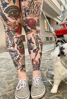 a woman's legs with tattoos on them and a small white dog standing next to her