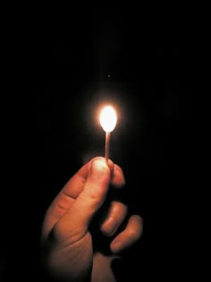 a person holding a lit matchstick in their hand with the light shining on them