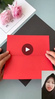 someone is holding up a red card with pink roses on it and the video below shows how to fold an envelope