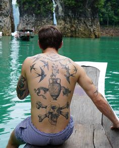 a man sitting on a dock with tattoos on his back