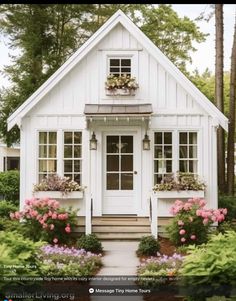 a small white house surrounded by flowers and greenery