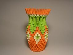 an orange and green vase sitting on top of a white table next to a gray wall