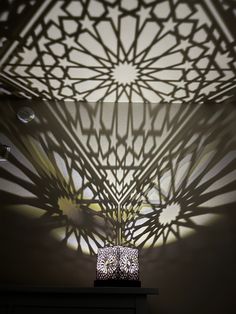 shadows cast on the wall and ceiling above a table with a vase in front of it