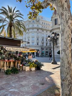 an open air market in front of a large white building with palm trees on the sidewalk