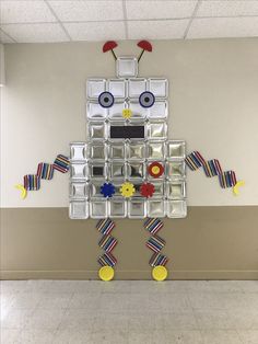 a robot made out of plastic containers on the wall in an empty room with tile flooring