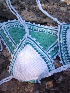 a green and white crocheted bag laying on the ground next to some rocks