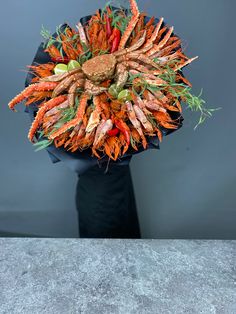 an arrangement of carrots and other vegetables in a black vase on a gray surface