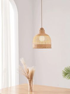 a wooden table topped with a vase filled with dried grass next to a light fixture