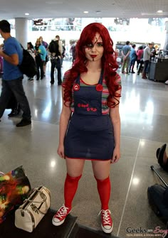 a woman with red hair and makeup standing next to luggage in an air port terminal