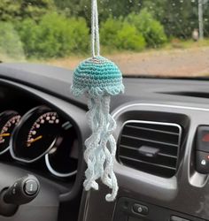 a car dashboard with a steering wheel hanging from it's center console, and a blue crocheted decoration on the dash