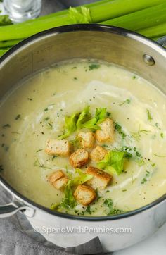 a pot filled with broccoli soup and croutons next to asparagus