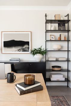 a wooden table topped with books and a coffee cup next to a shelf filled with books