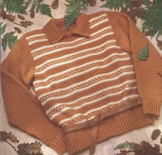 an orange and white sweater sitting on top of leaves