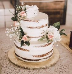 a three tiered cake with flowers and greenery on top is sitting on a table