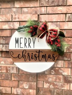 a merry christmas sign hanging on the side of a brick wall next to a wreath