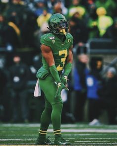 a football player standing on top of a field wearing a green uniform and holding a ball