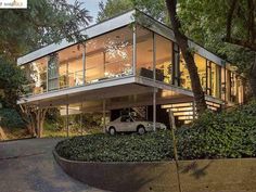 a car is parked in front of a modern house with trees and bushes around it