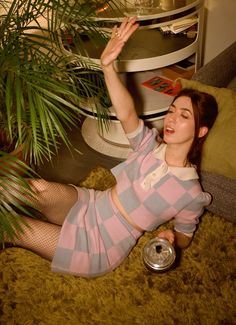 a woman laying on the floor next to a potted plant and holding a can