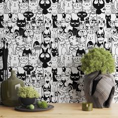 a black and white wallpaper with cats on it is next to a vase filled with green plants